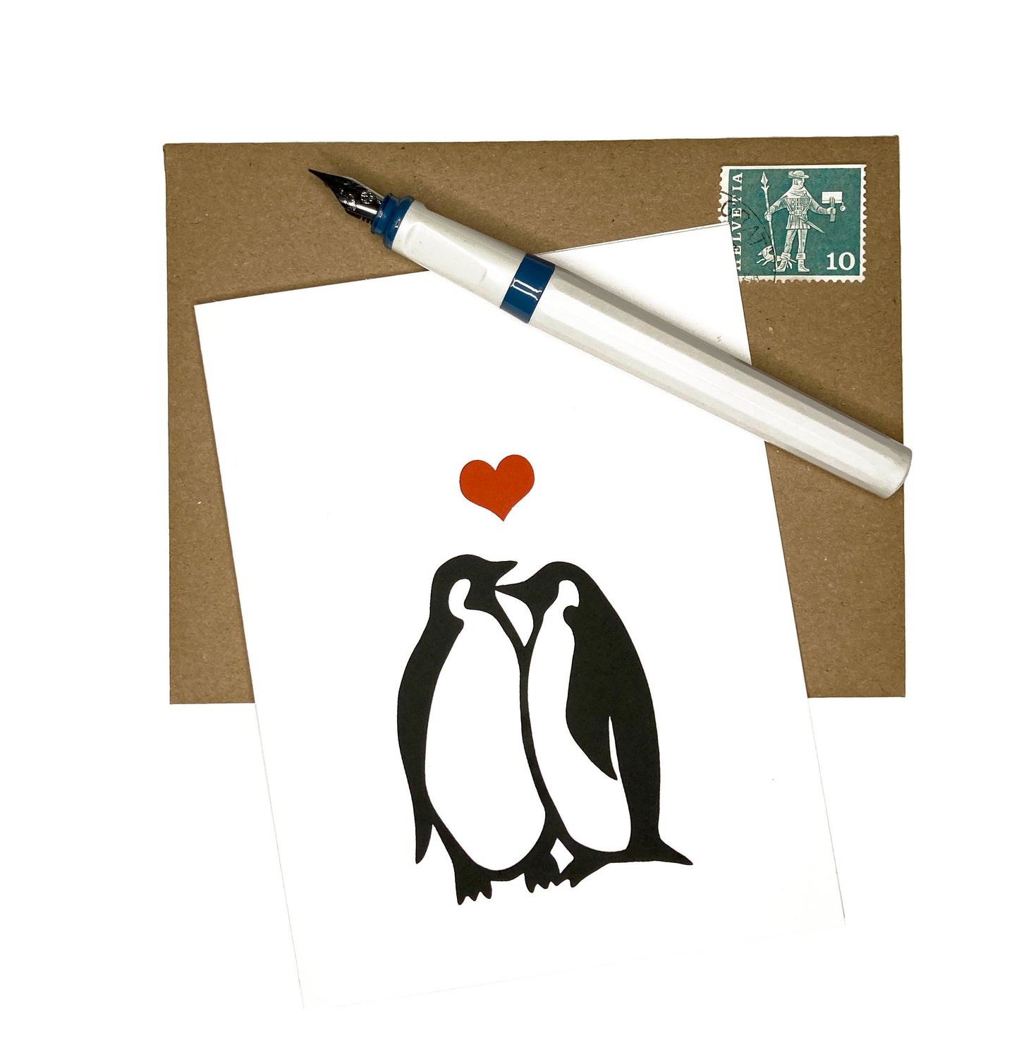 Our "Penguins In Love" card sits atop a brown stamped envelope with a pen